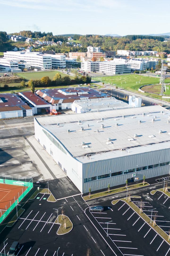 Großer Gebäudekomplex mit Parkplätzen, Tennisplätzen und umliegenden Sport- und Bürogebäuden in einer grünen Umgebung.