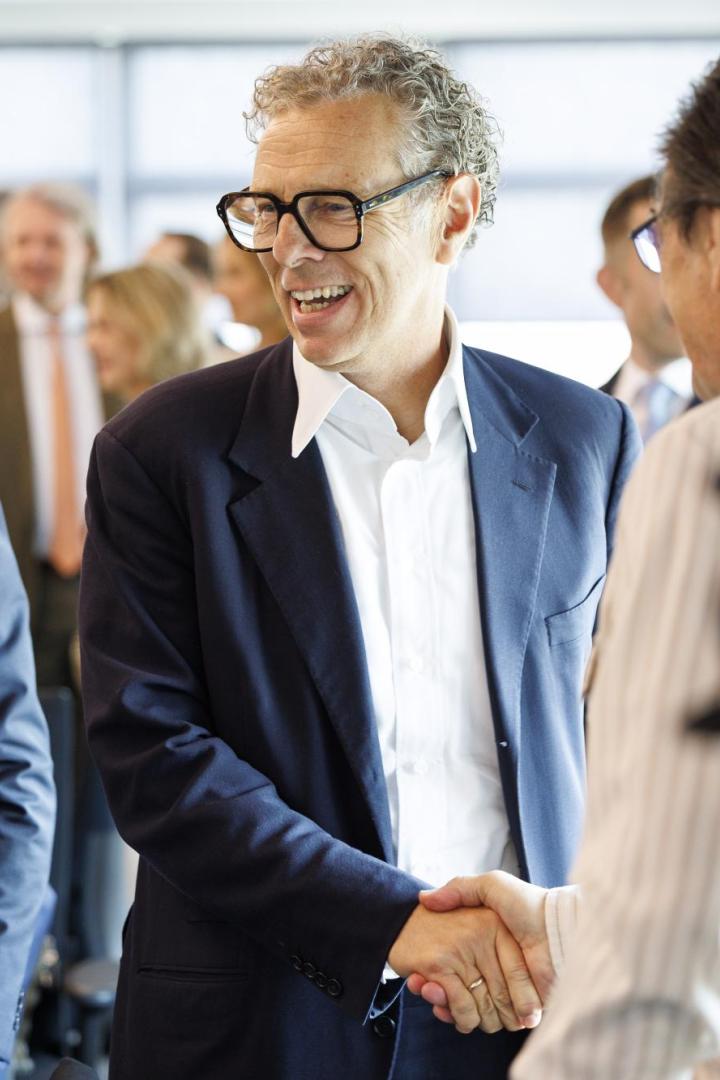 Mehrere Männer in Anzügen begrüßen sich freundlich per Handschlag in einem hellen Raum.