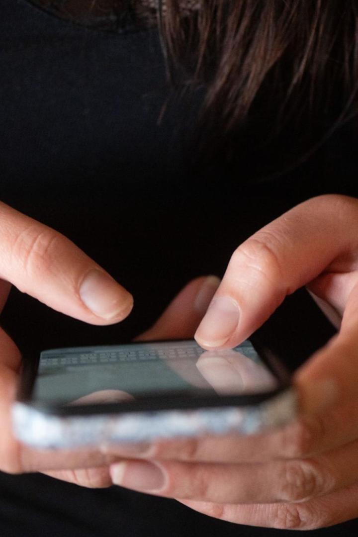 Eine Person tippt auf einem Smartphone, das sie in beiden Händen hält.