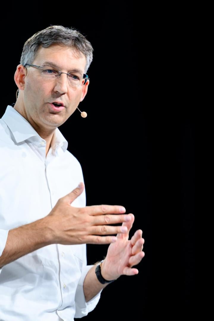 Markus Figl mit Brille und weißem Hemd gestikuliert vor einem schwarzen Hintergrund.