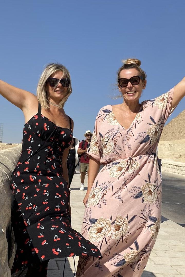 Zwei Frauen posieren vor den Pyramiden von Gizeh mit erhobenen Armen.