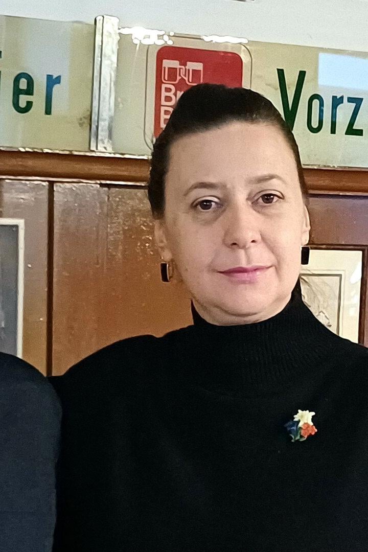 Zwei Frauen stehen nebeneinander in einem Raum mit Holzvertäfelung und alten Werbeschildern an der Wand.