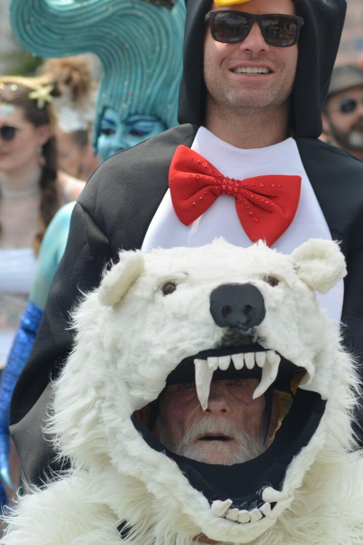 Mehrere Menschen in fantasievollen Kostümen, darunter ein Pinguin mit roter Fliege und ein Eisbärkostüm mit offenem Maul.