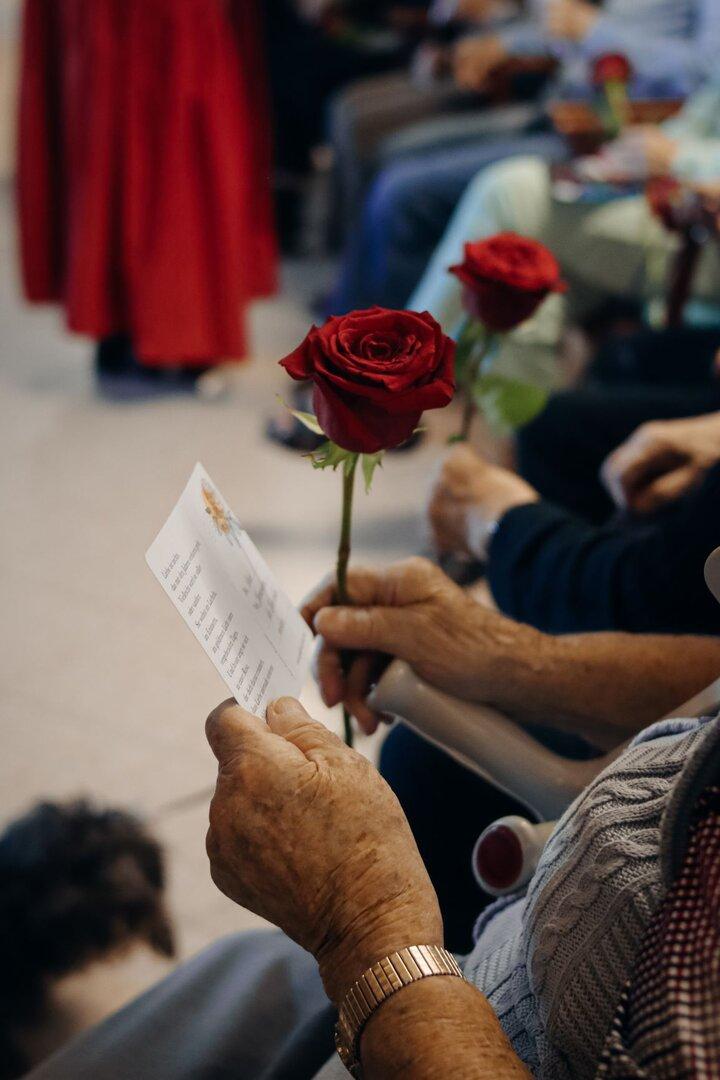 Eine ältere Hand hält eine Rose und eine Karte