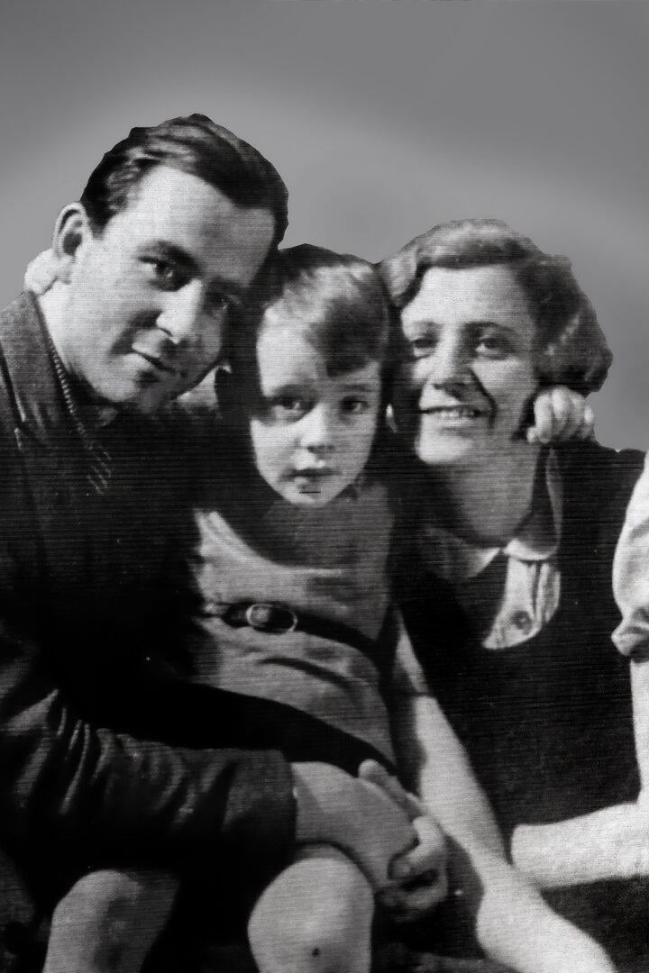 Ein Mann, ein Kind und eine Frau sitzen eng beieinander und lächeln gemeinsam in die Kamera.