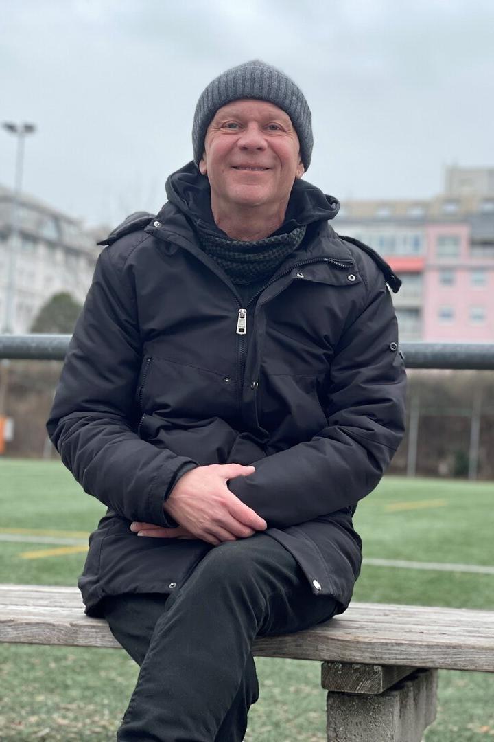 Helmut Emersberger sitzt auf einer Holzbank auf dem Sportplatz des WAT Brigittenau.