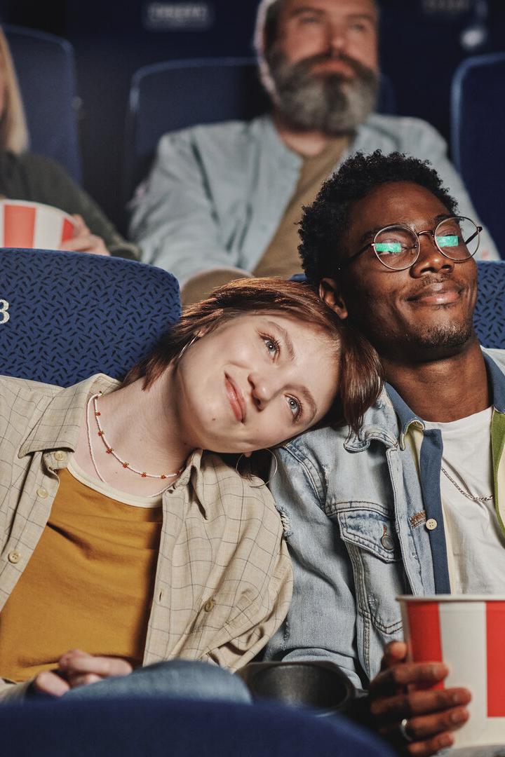 Ein junges Paar sitzt eng aneinandergelehnt im Kino und genießt Popcorn, umgeben von weiteren Zuschauern.