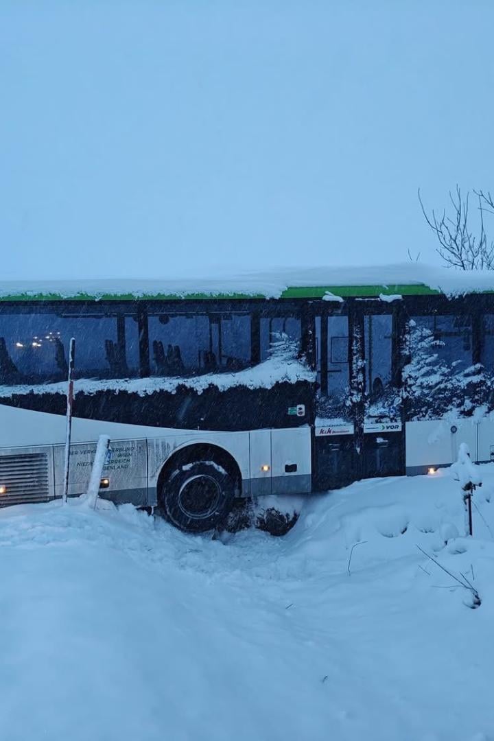 Ein Schulbus ragt senkrecht über den Straßengraben und in die dahinterliegende, schneebedeckte Wiese hinein.