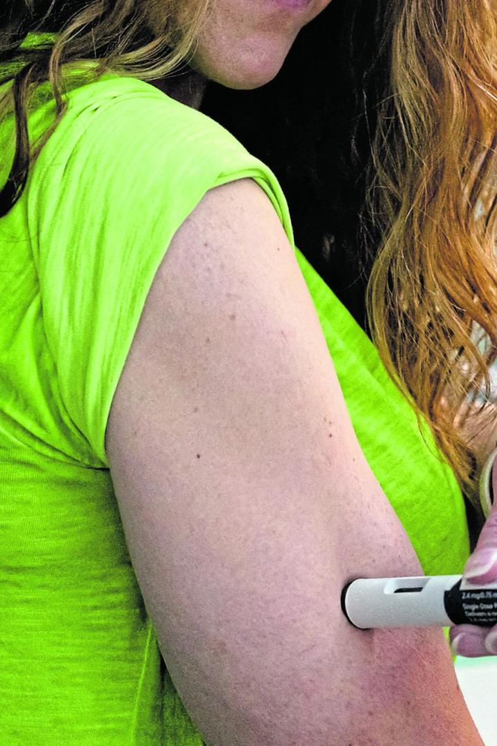 Eine Frau mit langen Haaren spritzt sich mit einem Injektionspen in den Oberarm.