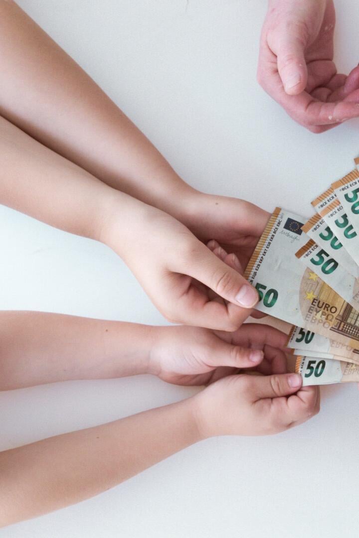 Ein Kind und eine ältere Person halten gemeinsam einen Fächer aus 50-Euro-Scheinen.