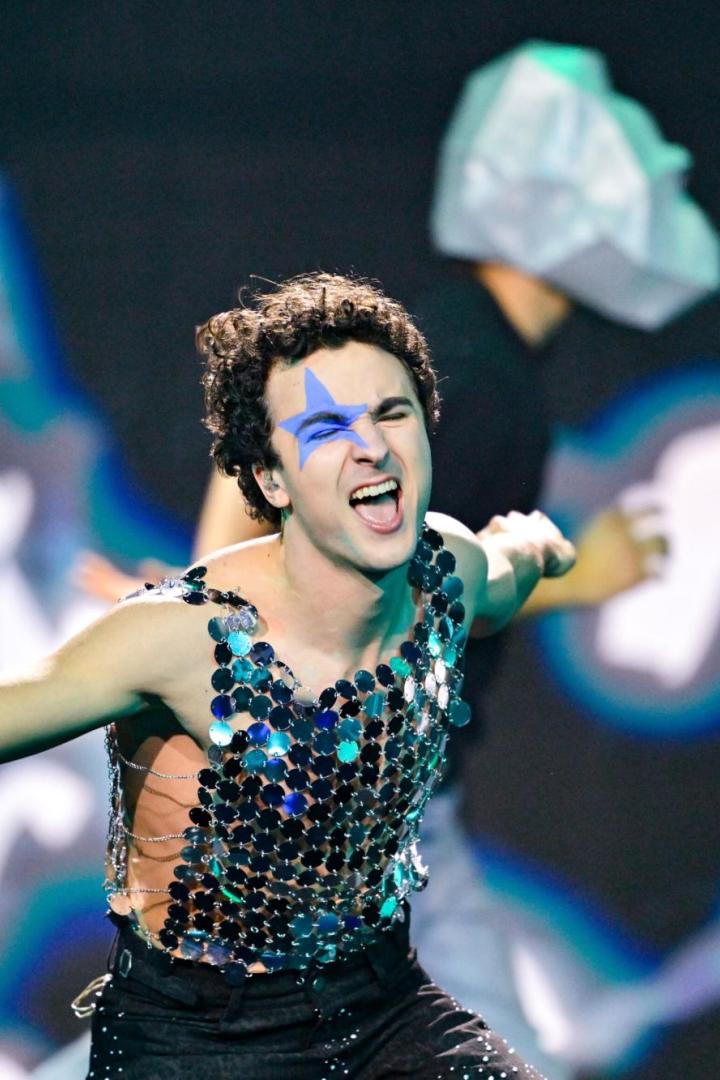 Ein Sänger mit blauem Stern im Gesicht performt mit glitzerndem Oberteil und Mikrofon auf der Bühne von Vienna Calling. 