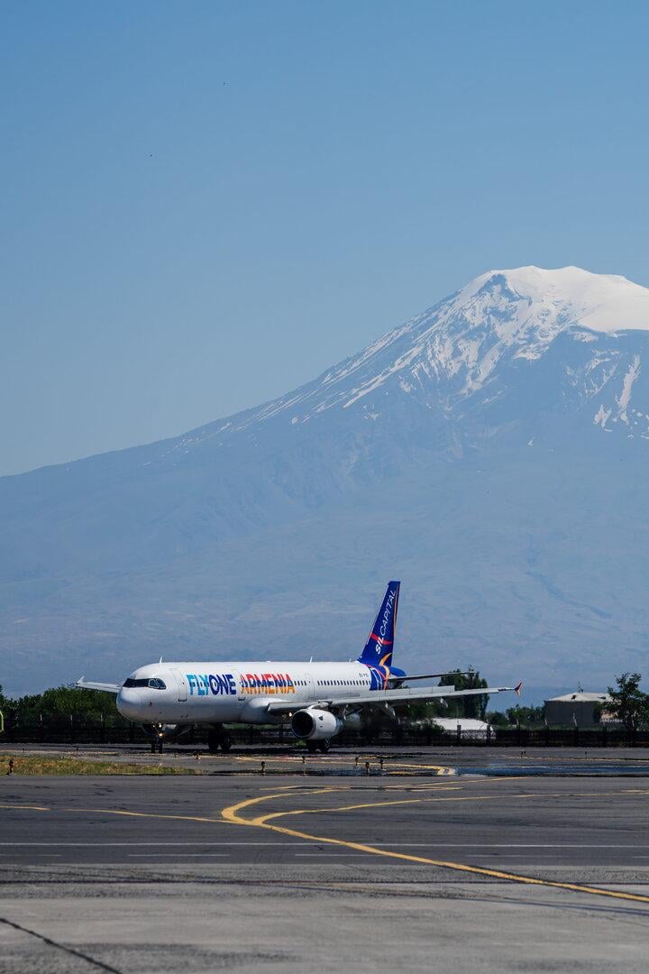 Ein Flugzeug von FlyOne Armenia steht vor einem schneebedeckten Berg auf einer Startbahn.