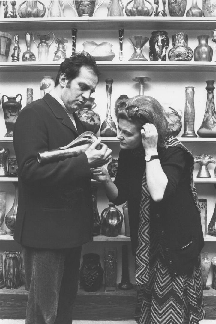 Ein Mann und eine Frau (Otto und Renee Schenk) betrachten eine Vase vor einem Regal voller Vasen.