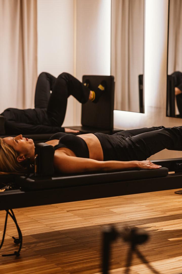 Zwei Frauen trainieren auf Pilates-Reformer-Jumpboard-Geräten in einem hellen Studio.