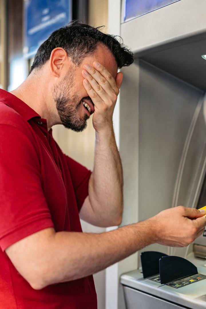 Mid-Adult Man Covering His Eyes Before Withdrawing Money Using A Credit Card At The ATM Machine