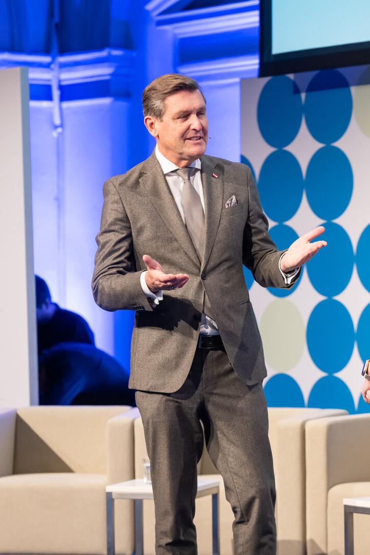 Ein Mann im Anzug und eine Frau unterhalten sich auf einer Bühne mit moderner, blau-weißer Kulisse.