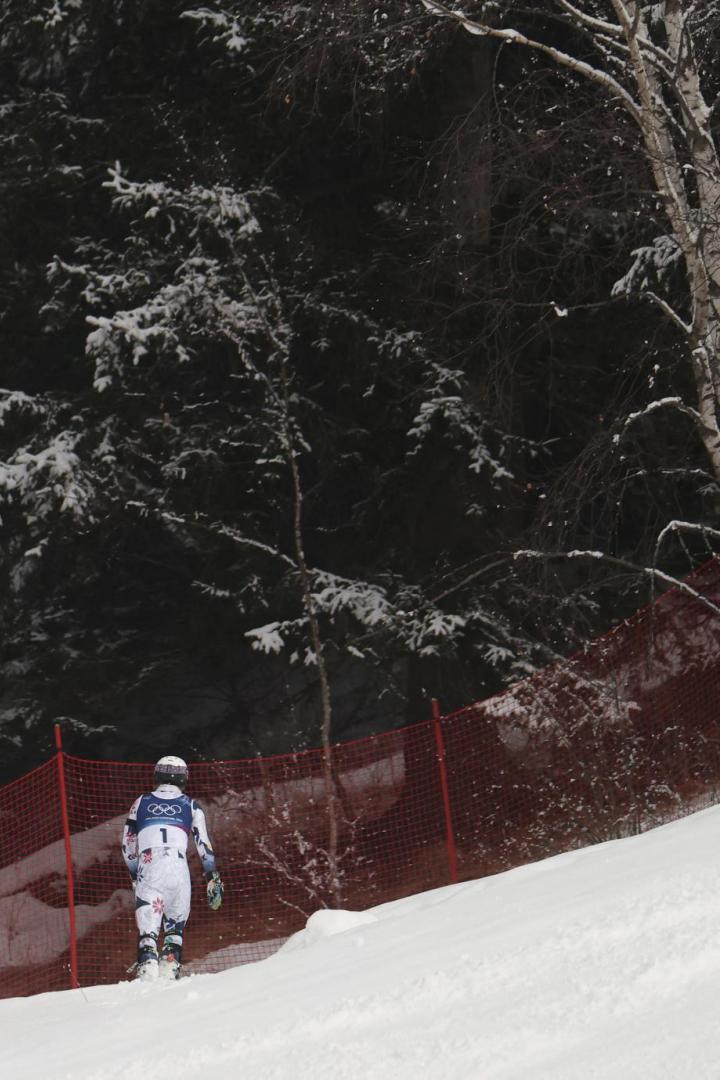 Ein Skifahrer in Rennanzug steht vor einem roten Sicherheitsnetz im verschneiten Wald.