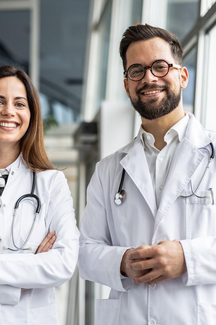 Two smiling doctors wearing white coats and stethoscopes in hospital corridor