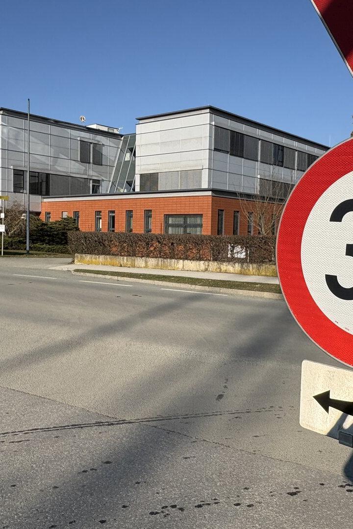 Ein 30 km/h-Schild steht am Straßenrand vor einem modernen Bürogebäude.