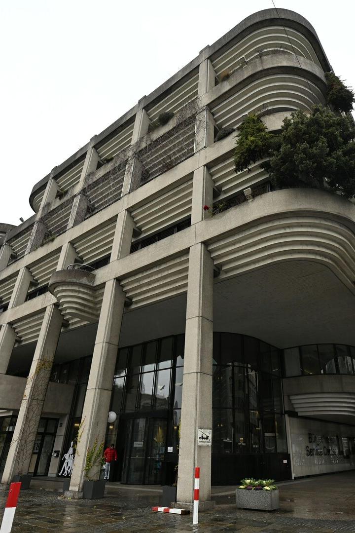 Ein großes, modernes Gebäude mit vielen Balkonen und Säulen steht an einer Straße.