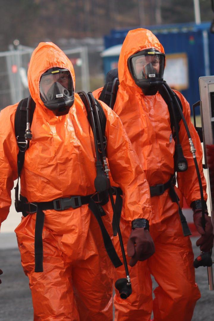 Zwei Personen in orangen Schutzanzügen mit Schutzmasken