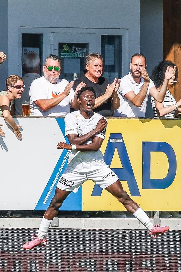 Ein Fußballspieler (Alieu Conateh) jubelt vor begeisterten Fans, die am Spielfeldrand klatschen und jubeln.