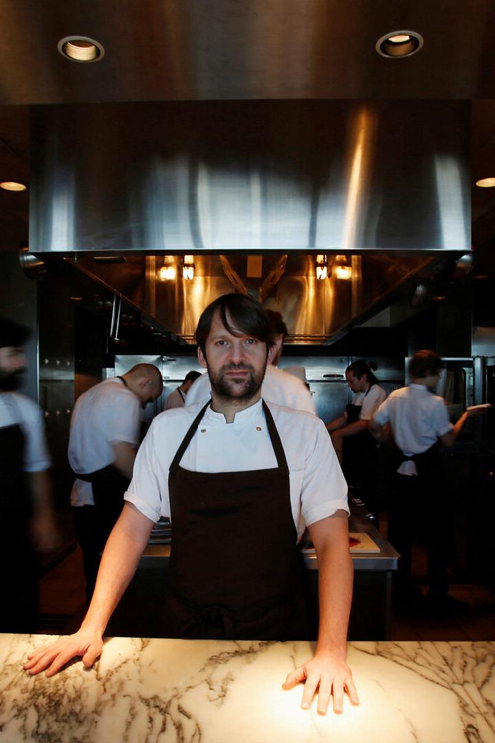 Starkoch und Noma-Chef René Redzepi steht an einer Marmorarbeitsfläche, während mehrere Köche im Hintergrund arbeiten.