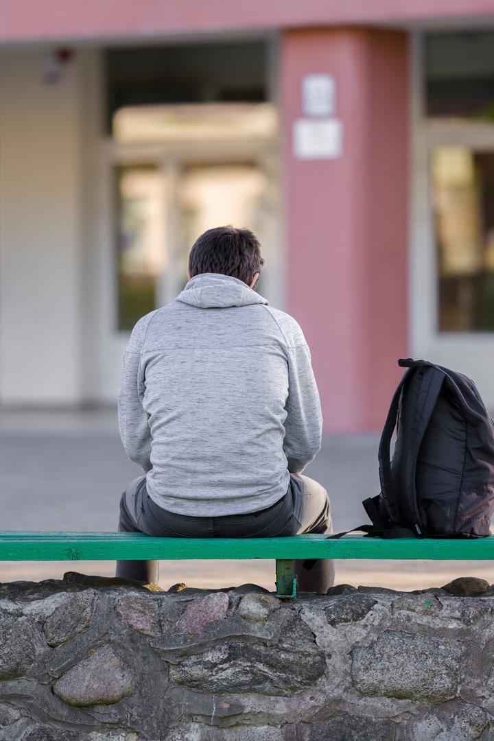 One young man sitting on bench at school yard. Break time. Back view.