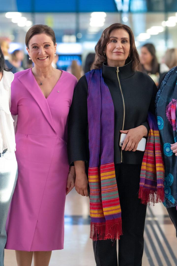 Sechs Frauen stehen nebeneinander und lächeln in einer hellen, modernen Umgebung.