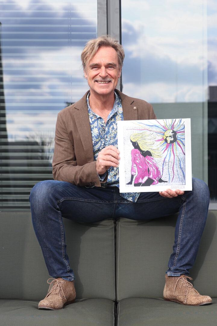 Ein Mann sitzt auf einem Sofa und hält ein Bild mit einer farbenfrohen Illustration.