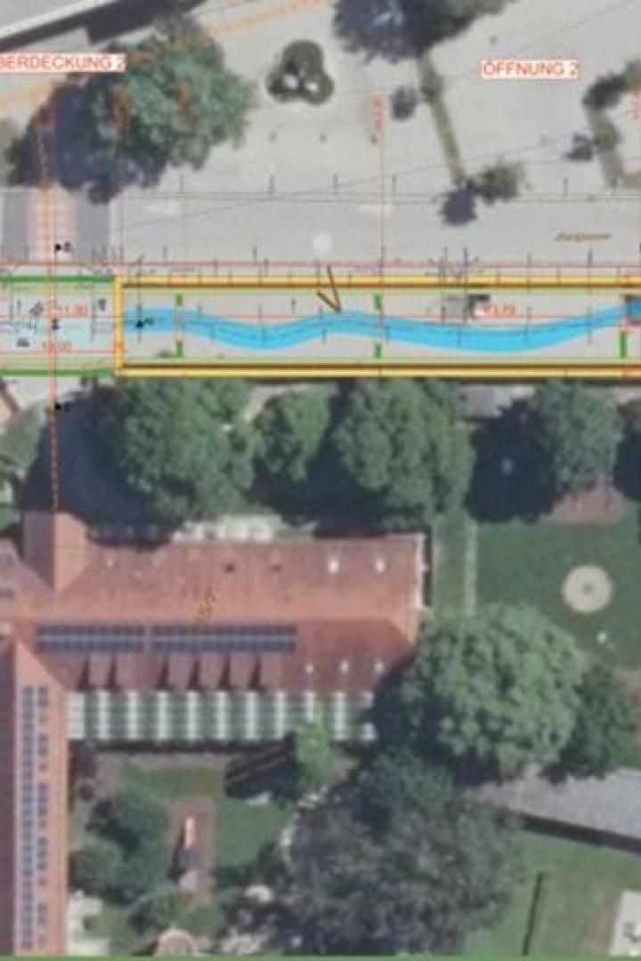 Luftaufnahme eines Stadtgebiets mit eingezeichnetem geplanten Wasserlauf, Straßen und Gebäuden sowie einem Freibad mit Becken.