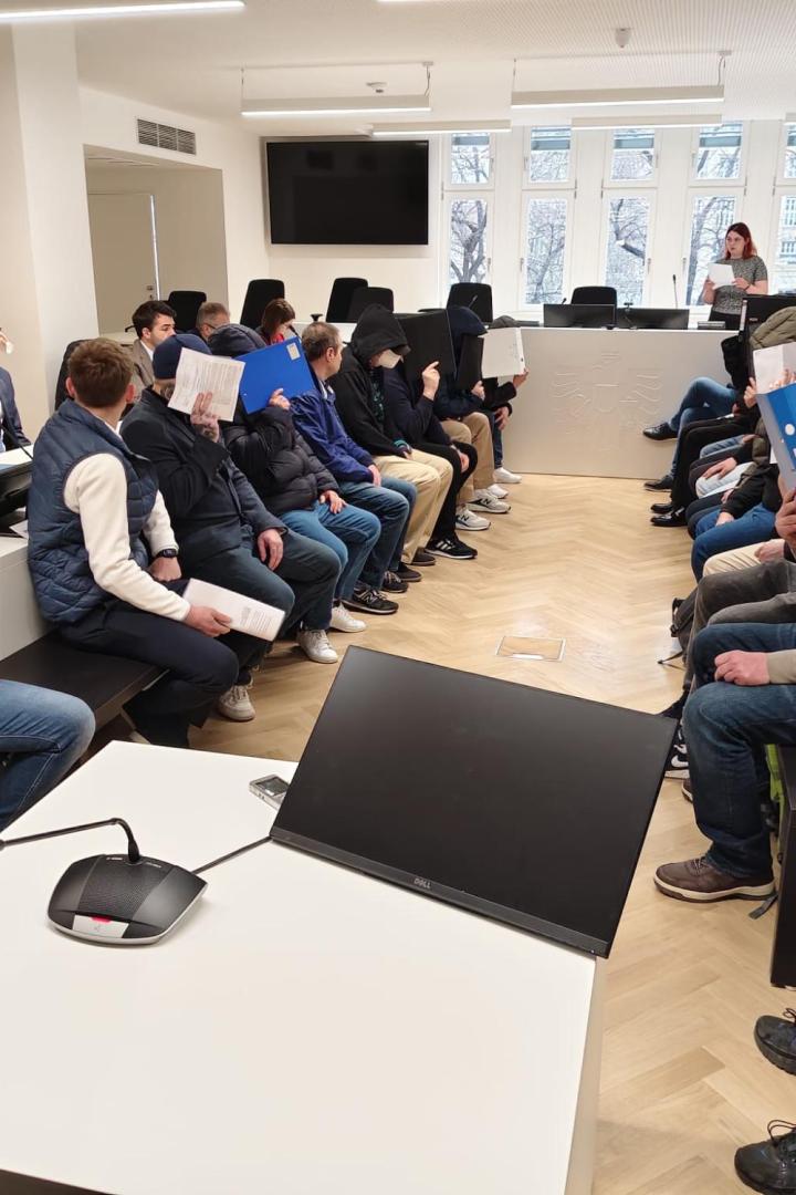 Angeklage halten sich Aktenordner vors Gesicht.