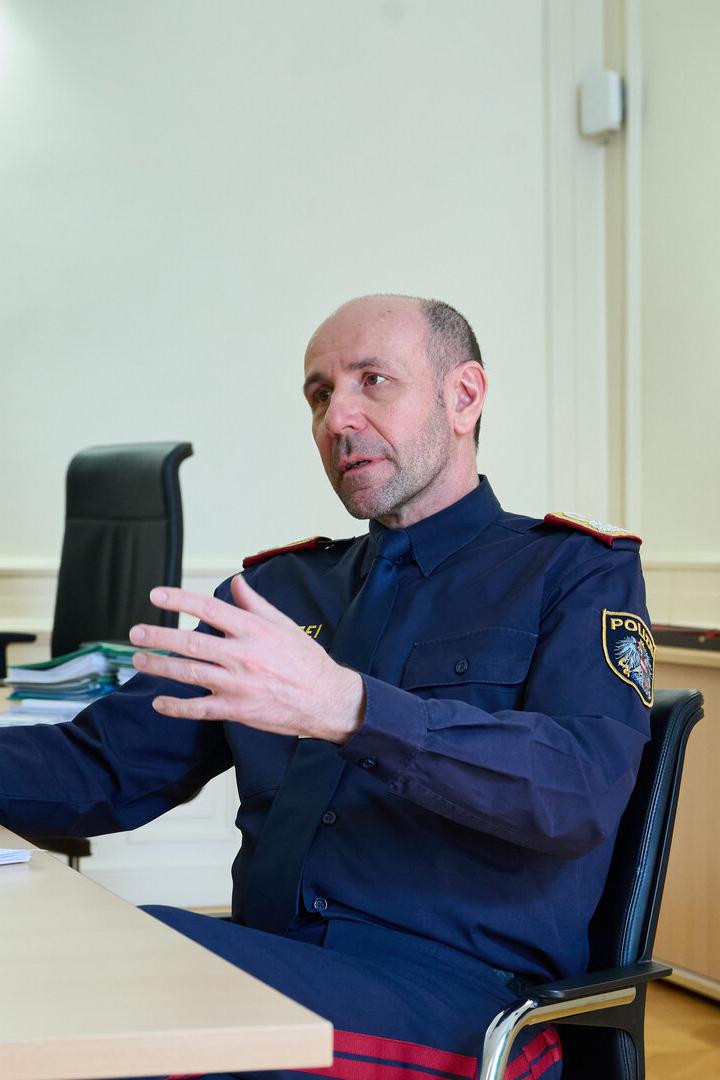 Ein Polizist in Uniform sitzt an einem Schreibtisch und gestikuliert während eines Gesprächs.