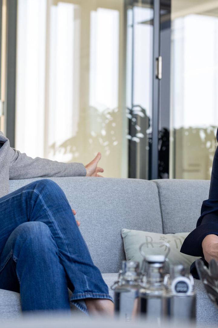 Zwei Personen sitzen auf einem Sofa und führen ein Gespräch in einem modernen Büro mit Glaswänden.