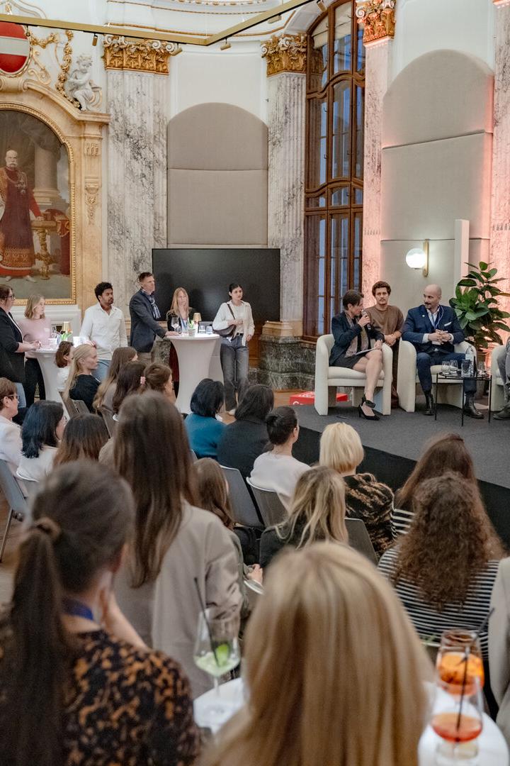 Eine Podiumsdiskussion mit mehreren Teilnehmenden findet in einem prunkvollen Saal vor zahlreichem Publikum statt.