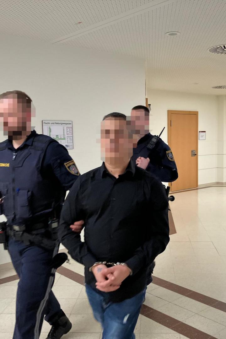 Ein Mann in Handschellen wird von zwei Polizisten durch einen Gerichtsflur geführt.