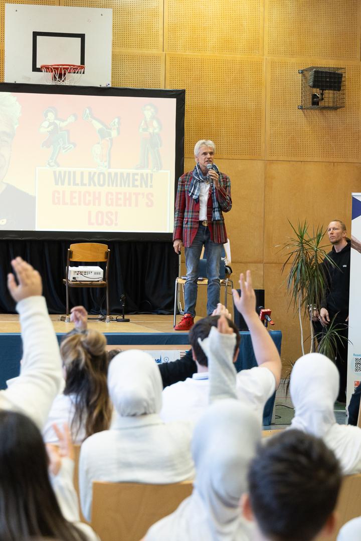 Thomas Brezina auf der Bühne, mehrere Jugendliche im Publikum zeigen auf. 