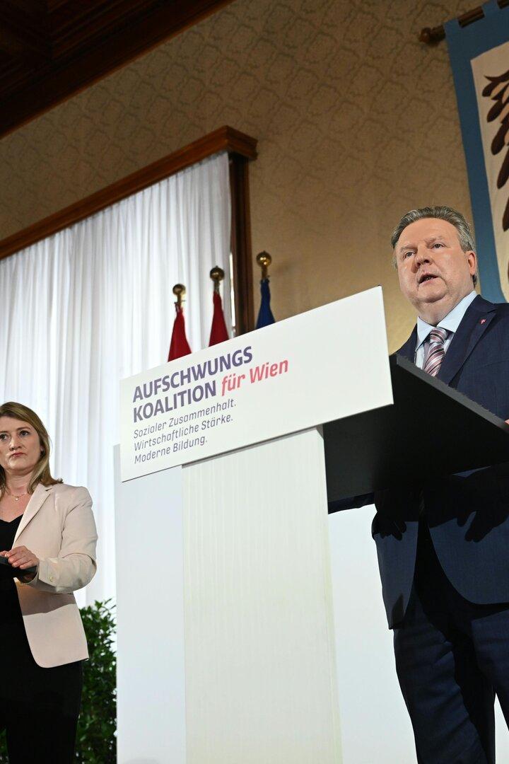 Eine Frau und ein Mann stehen an Rednerpulten mit der Aufschrift "Aufschwungs Koalition für Wien".