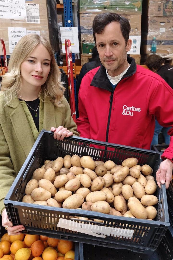 Zwei Personen halten eine Kiste mit Kartoffeln in einem Lagerraum mit Lebensmitteln.