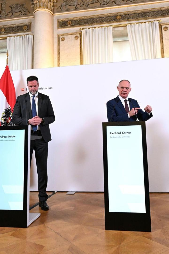 Drei Männer, darunter Gerhard Karner, stehen vor Flaggen und Bildschirmen bei einer Pressekonferenz.