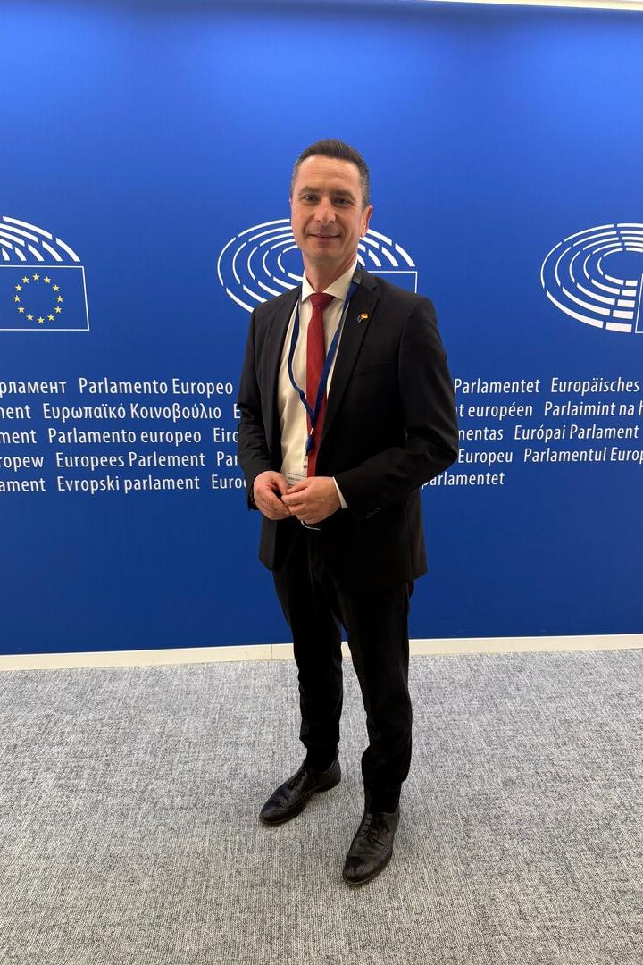 Ein Mann im Anzug steht vor einer blauen Wand mit Logos und Schriftzügen des Europäischen Parlaments.