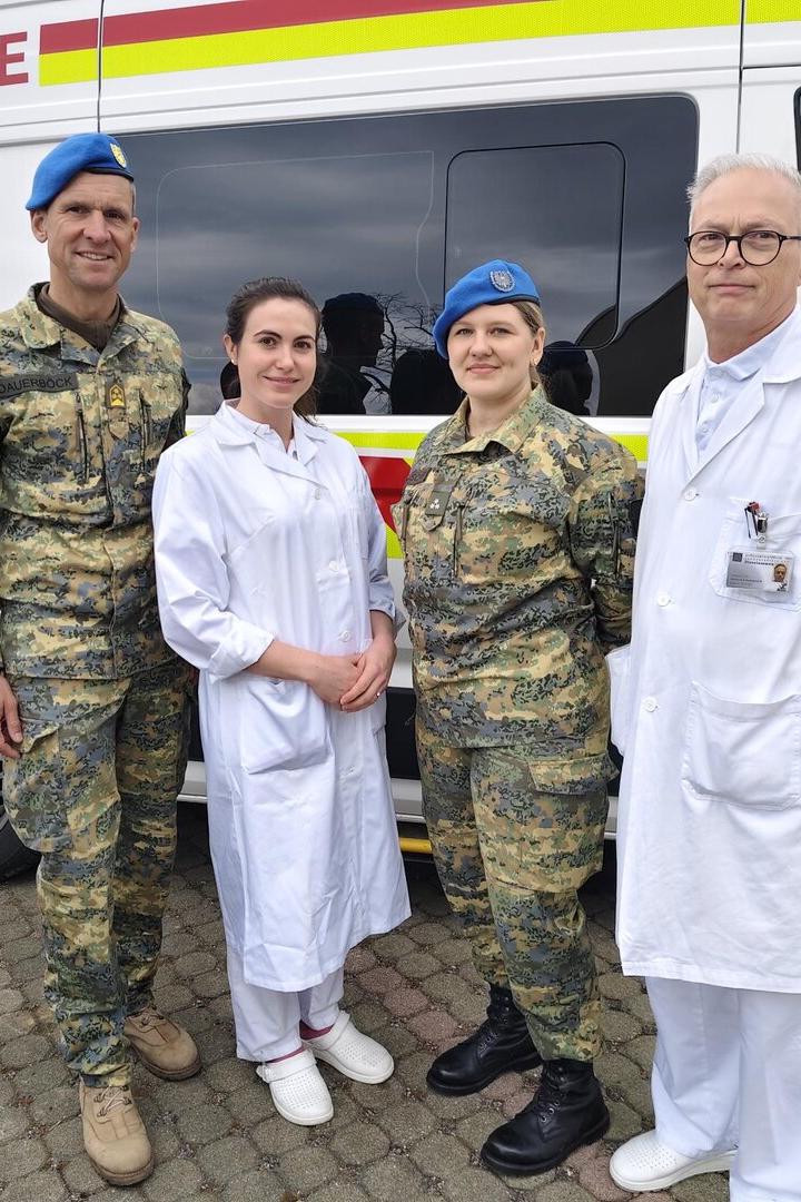 Zwei Personen in Militäruniform und zwei in weißer Kleidung stehen vor einem Rettungswagen mit der Aufschrift „Bundesheer“.