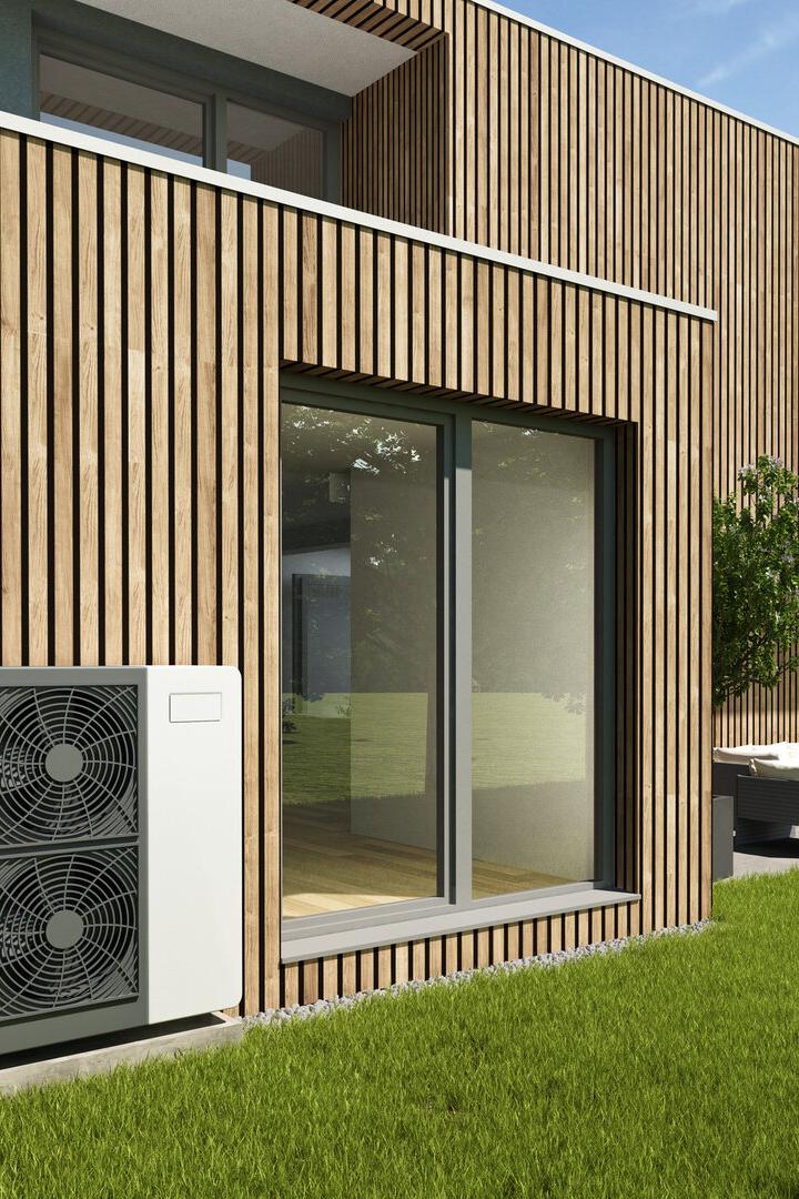 Ein modernes Haus mit Holzfassade, Wärmepumpe und großem Fenster zum Garten.