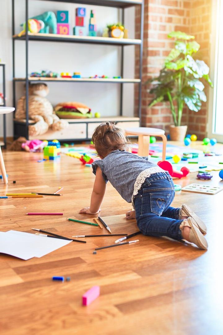 Beautiful toddler crawling on the floor around lots of toys at kindergarten