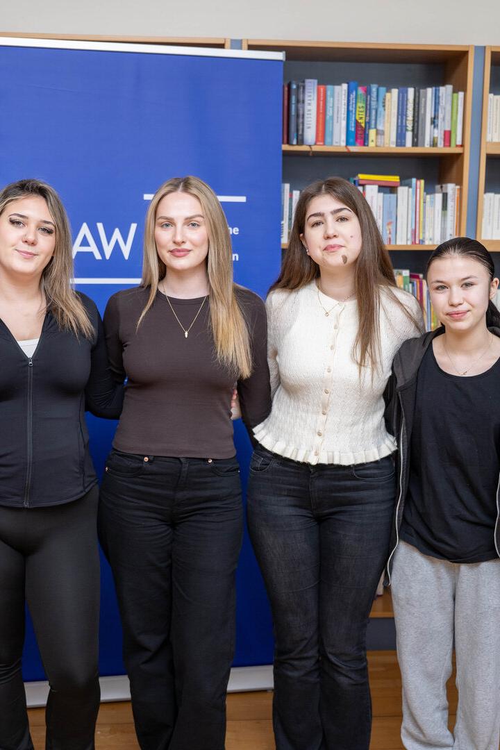 Sechs Personen stehen lächelnd vor Bücherregalen und einem blauen Aufsteller nebeneinander.