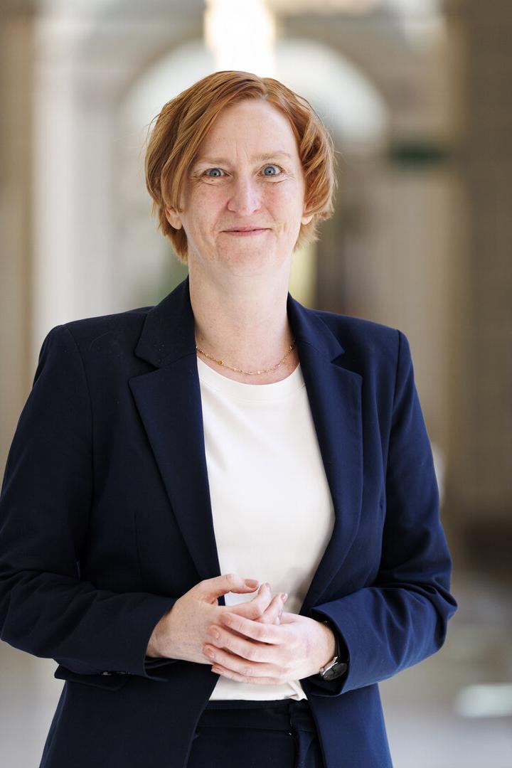 Elke Habel-Torsch mit kurzem, rötlichem Haar trägt einen dunkelblauen Anzug und steht in einem hellen Flur mit Säulen im Wiener Rathaus.