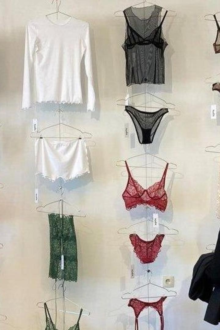 Verschiedene bunte Dessous und Oberteile hängen an einer Wand, während drei Personen davor stehen.