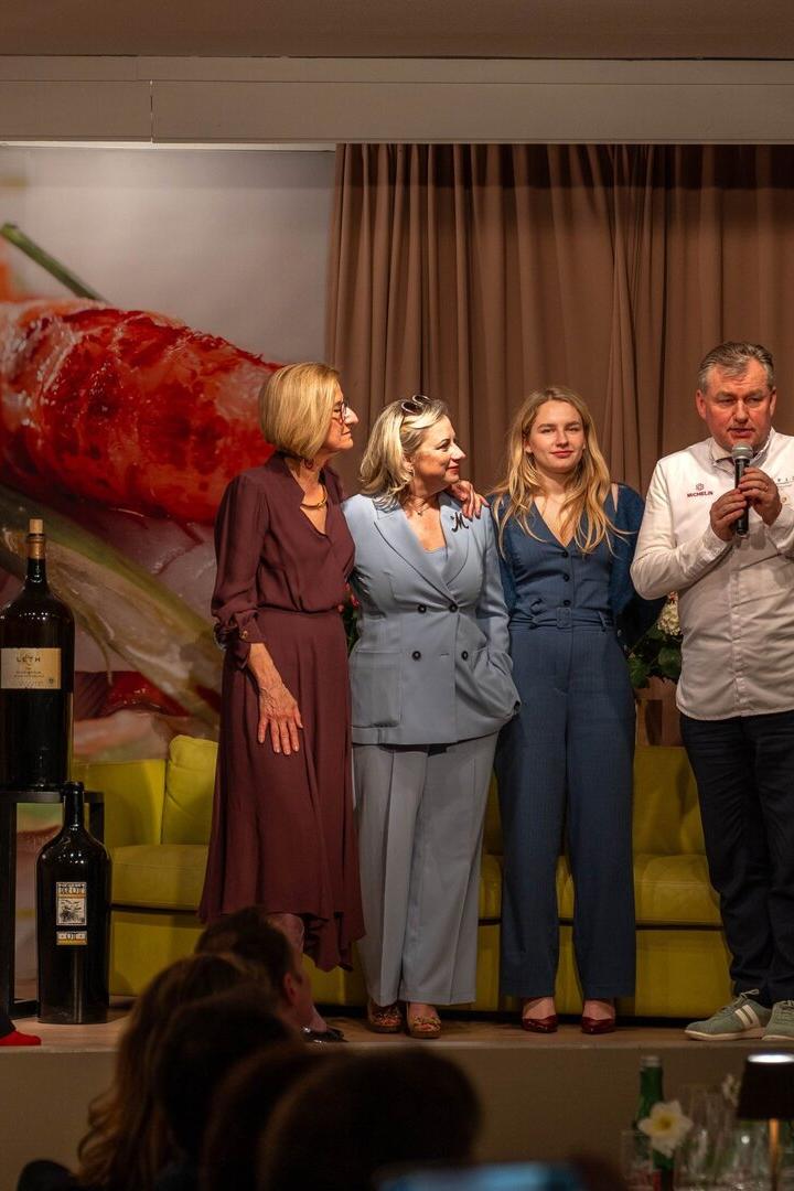 Fünf Personen stehen auf einer Bühne vor einem großen Essensmotiv, während eine Person ins Mikrofon spricht.