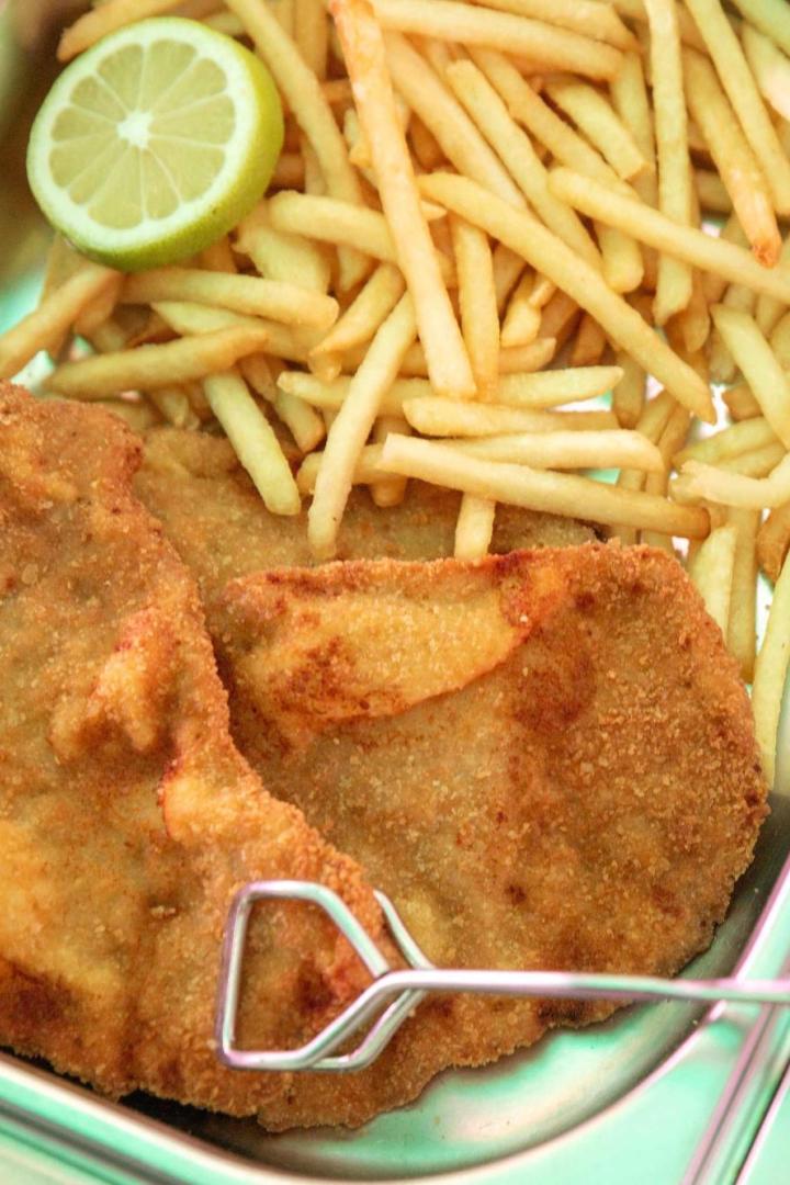 In einer Metallschale liegen Schnitzel, Pommes und eine Zitronenscheibe.