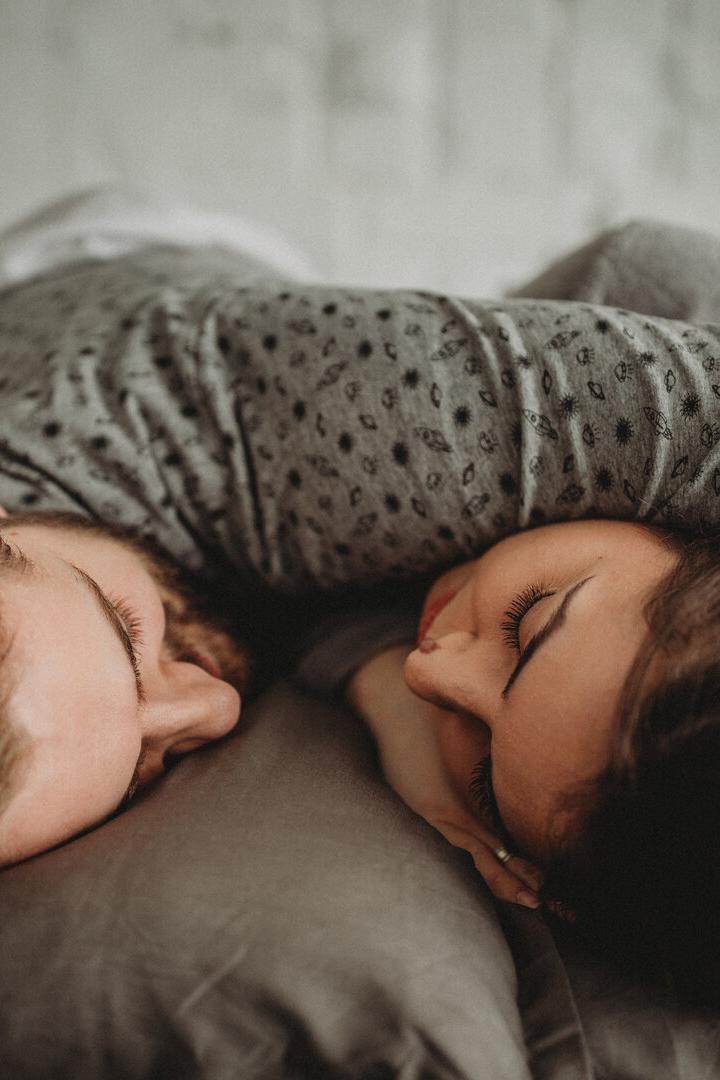 Zwei Menschen liegen eng umarmt auf einem Kissen und schlafen mit geschlossenen Augen nebeneinander.